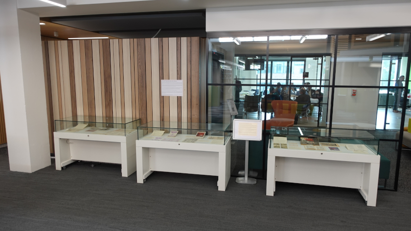 Exhibition featuring 3 exhibition cabinets and poster stand next to a wall.