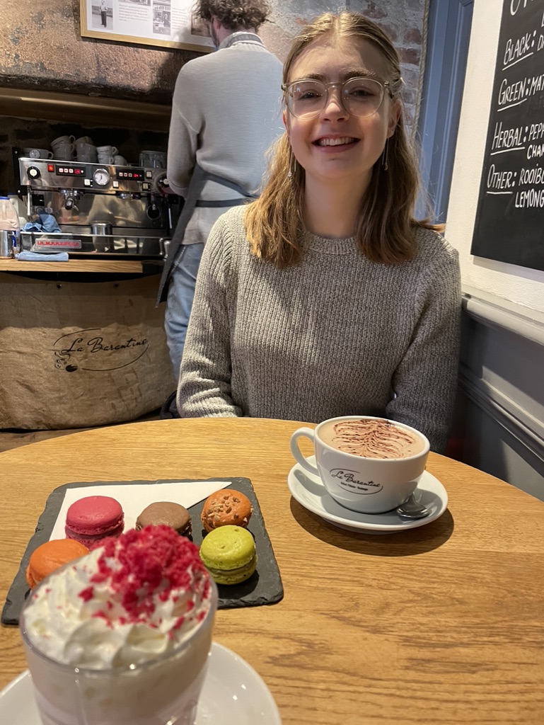 An image of Amelia, Amelia is sat in a cafe wearing a grey jumper