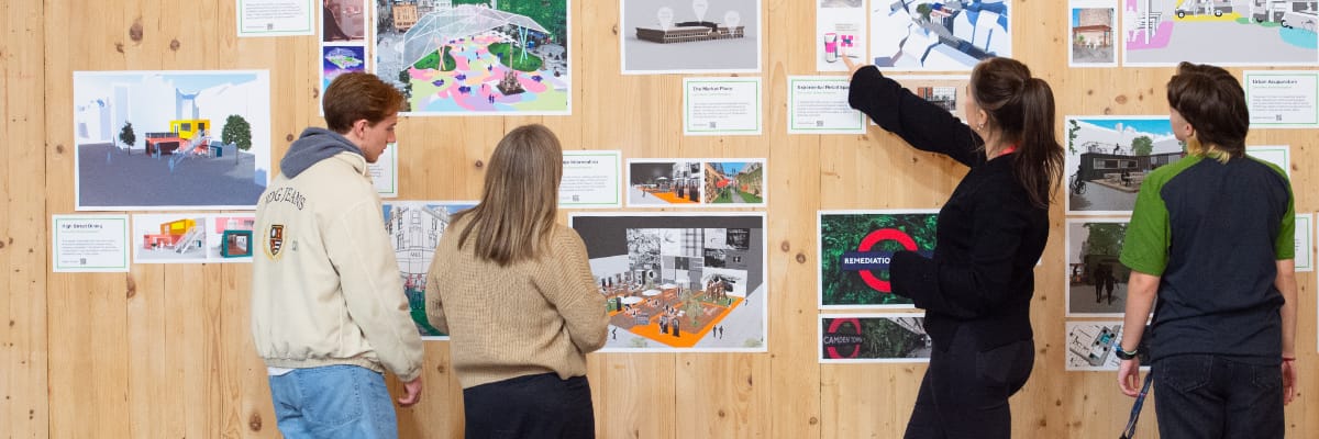 Four students stand at a wall looking at various drawings stuck to the wall.