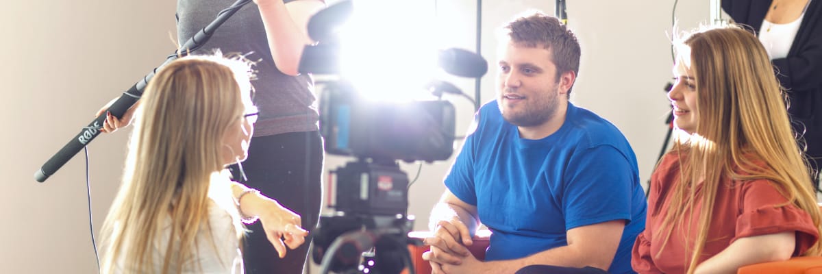 A film crew surrounds two people on a sofa.