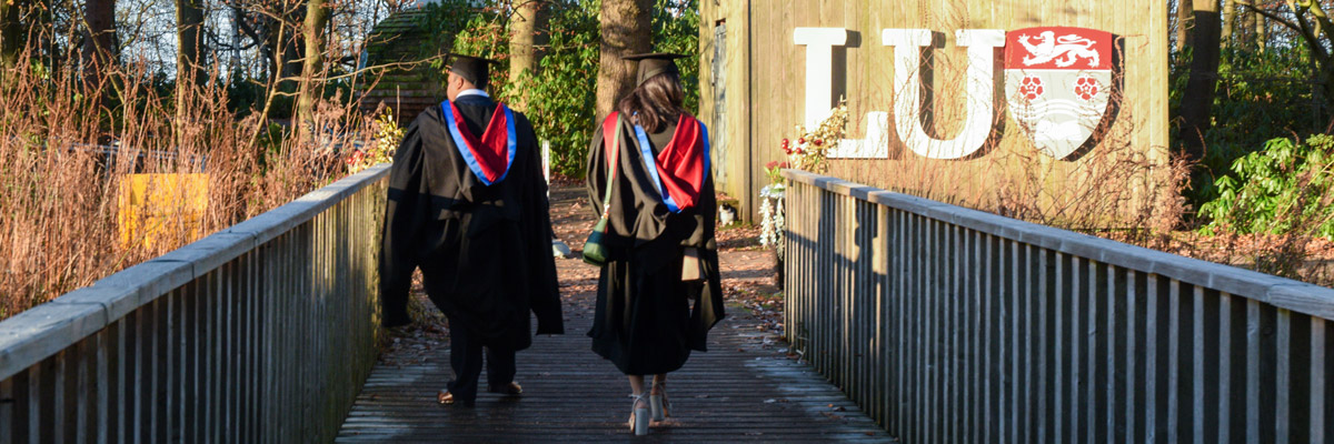 Students wearing graduation gowns in front of and LU sign walking away from the camera