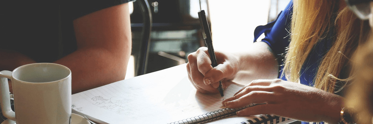 Photograph of person with blonde long-hair taking notes at a meeting