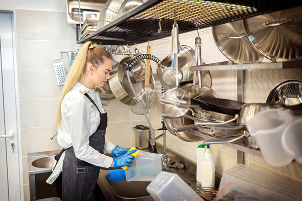 A woman washing dishes using a sponge in a restaurant kitchen.