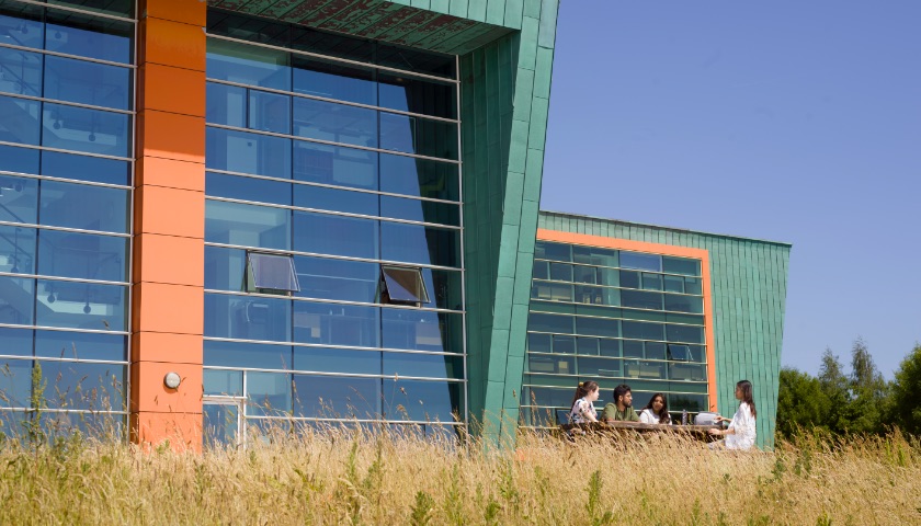 Students sit at a picnic bench in front of the Infolab building