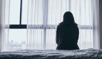 A woman sitting on a bed looking out of a window.
