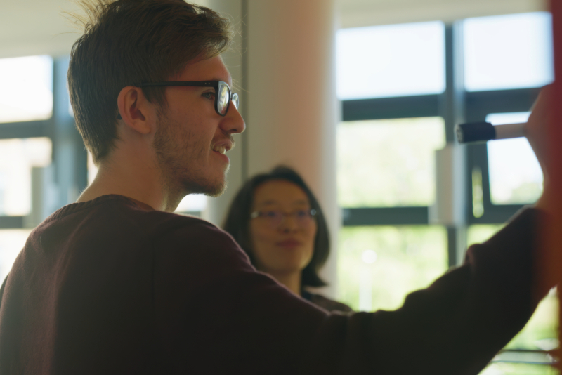 A student working with a supervisor on a whiteboard