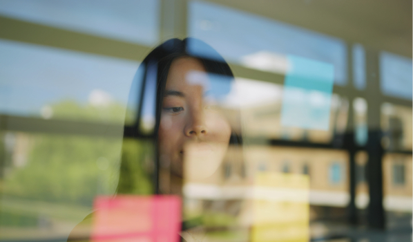 Student writing on post-it notes on glass