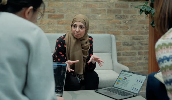 A woman talking to two other people presenting from a laptop.