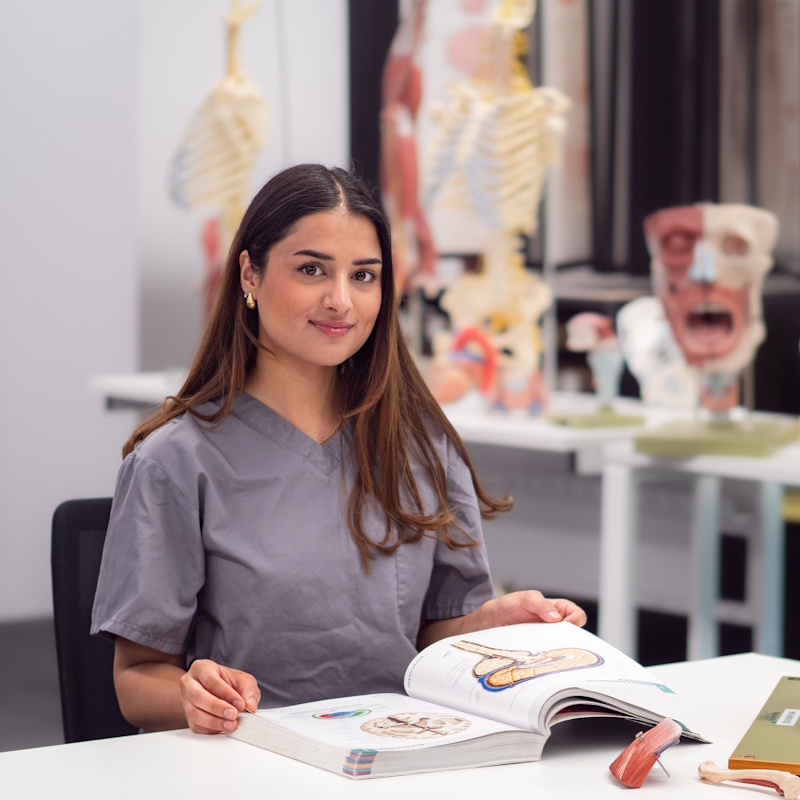 Medicine student Isra wearing grey scrubs, reading an anatomy text book.