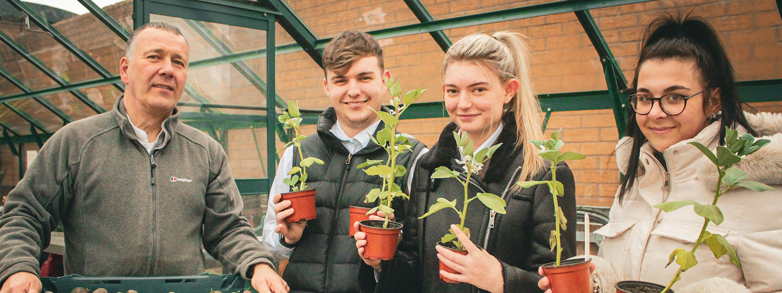 Secondary school students pose with potted plants in a greenhouse