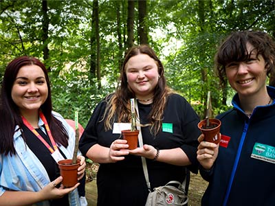 Three people in the woods holding seedlings in tubs