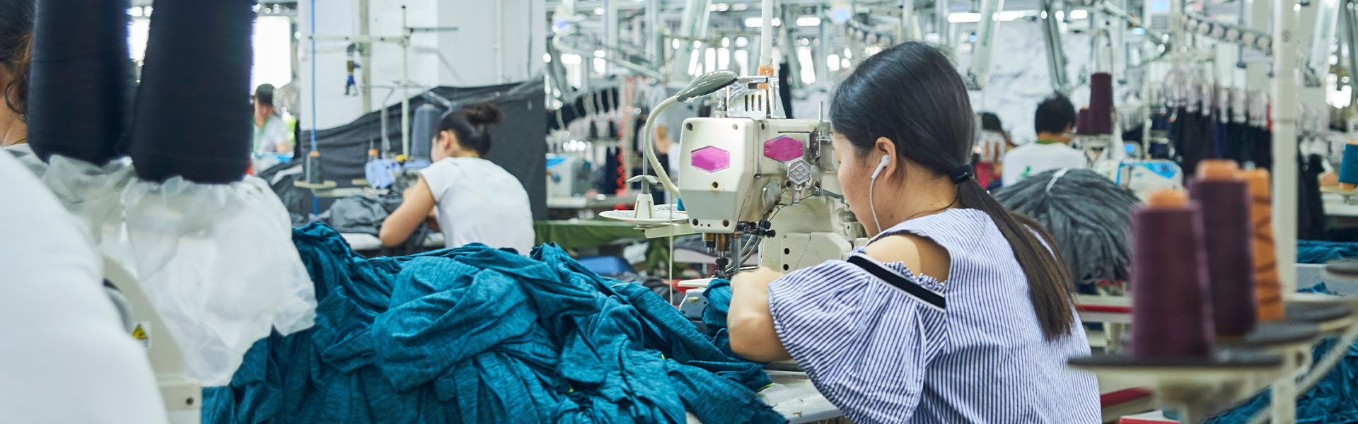 A woman sits in a large warehouse working a sewing machine.