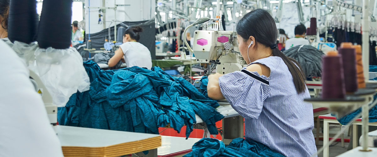 A woman is working at a sewing machine in a large factory.