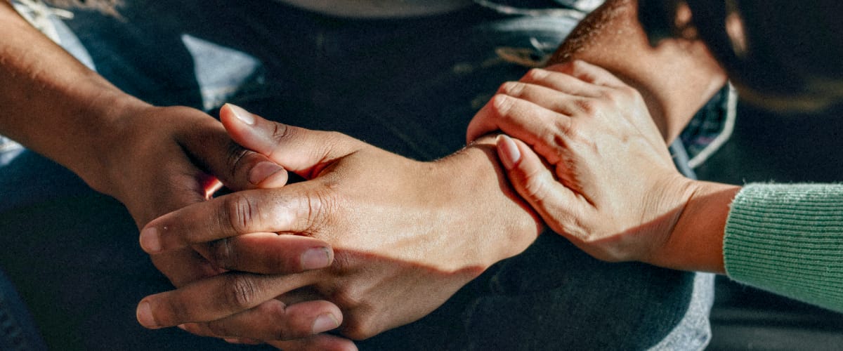 A person clasps their hands while another person consoles them.