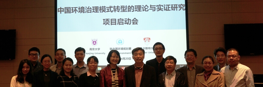 Fifteen people in semi-dark room lined up in front of a screen with Chinese characters