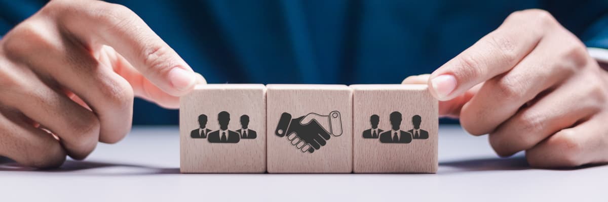 3 wooden building blocks with handshake and people icons held together by someone's fingertips