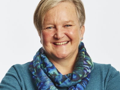 Woman smiling, against black background: Professor Jan Bebbington