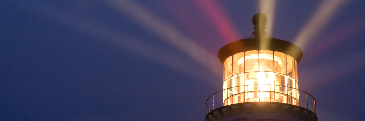 A lighthouse emitting beams of light against a midnight blue sky