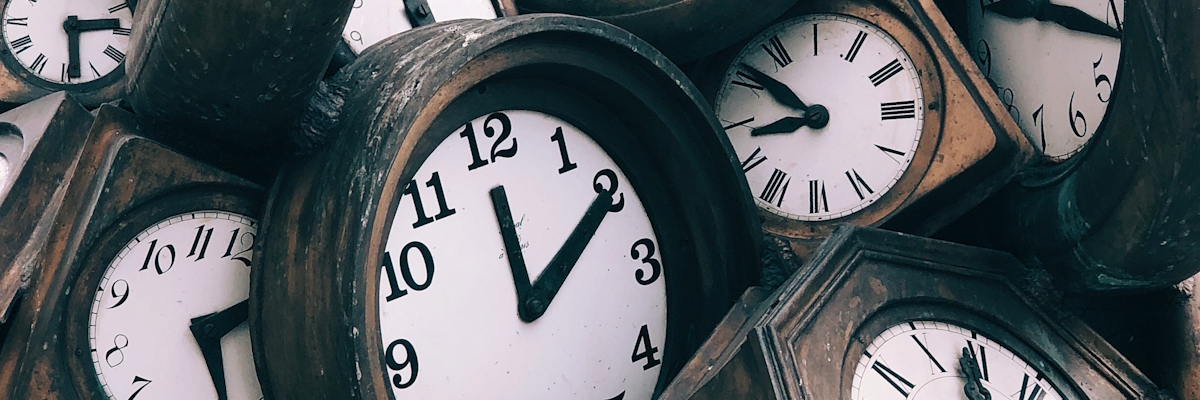 A pile of tumbling wood-framed clocks. Photo by Jon Tyson on Unsplash.