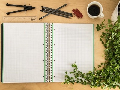 An open notebook with pens and a coffee mug at the side
