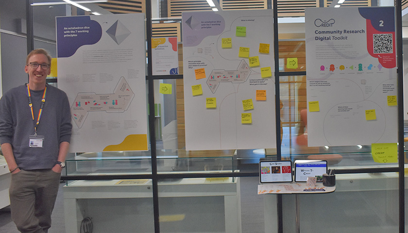 Picture of one of the researchers on the RRP project besides posters of the exhibition 