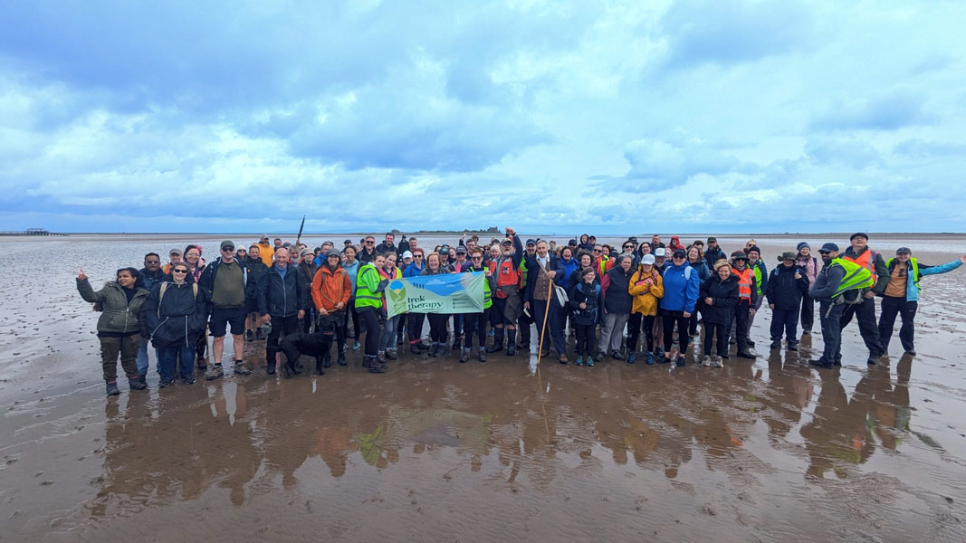 A large group of people on Morecambe Bay beach holding a banner
