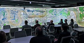 Adults sitting at tables looking at a wall of tv screens displayed like a cinema