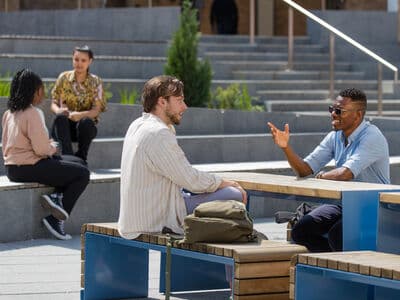 Two student sat at a bench table chatting in the sunshine