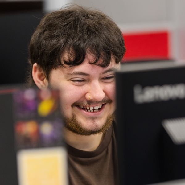 Student smiling whilst looking at a computer monitor