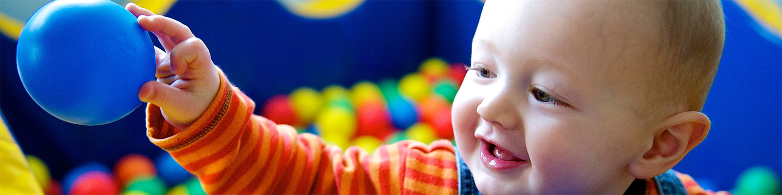 Smiling baby reaching for a blue toy ball