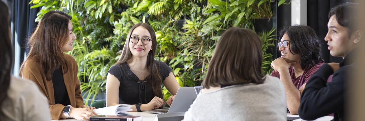 Students sit around a table in the library infront of the green living wall