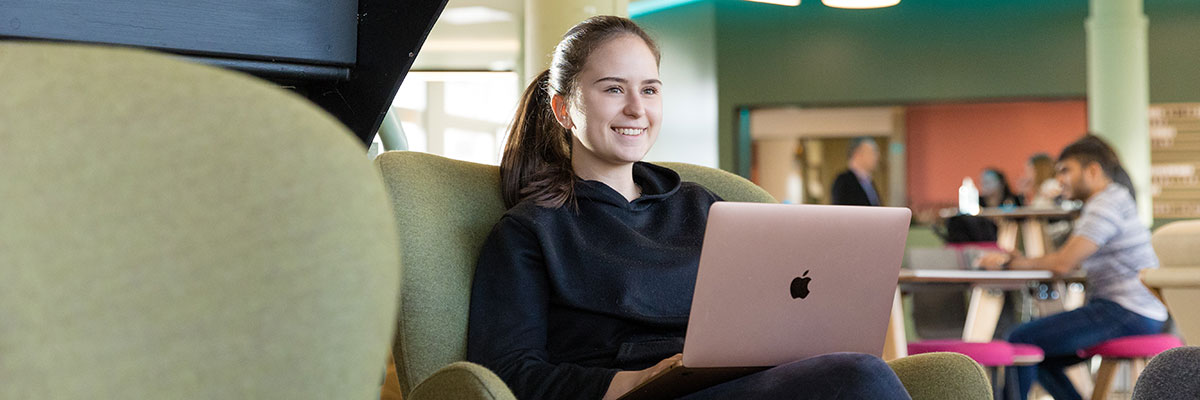 A student sits in an easy chair using a laptop