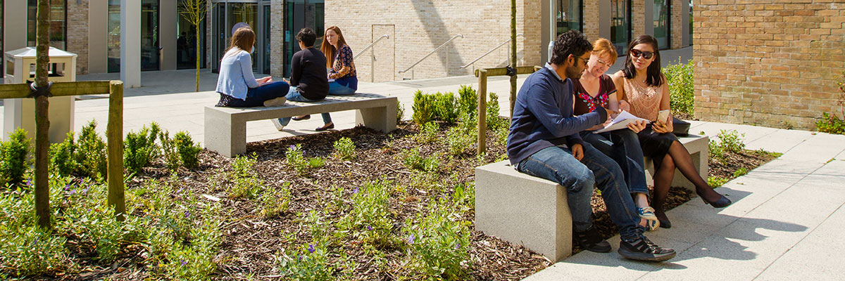 Students sitting on a bench in the sunshine outside a modern university building