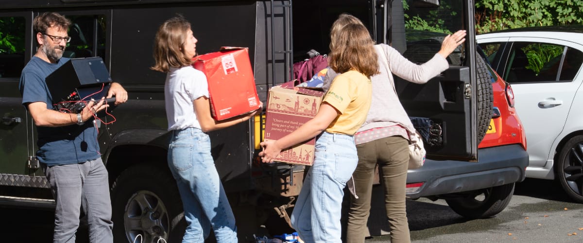 A family unload boxes from the back of a car.