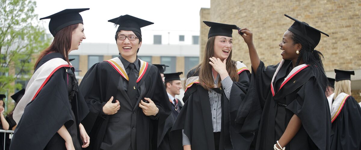 Four students celebrate their graduation whilst standing in caps and gowns.