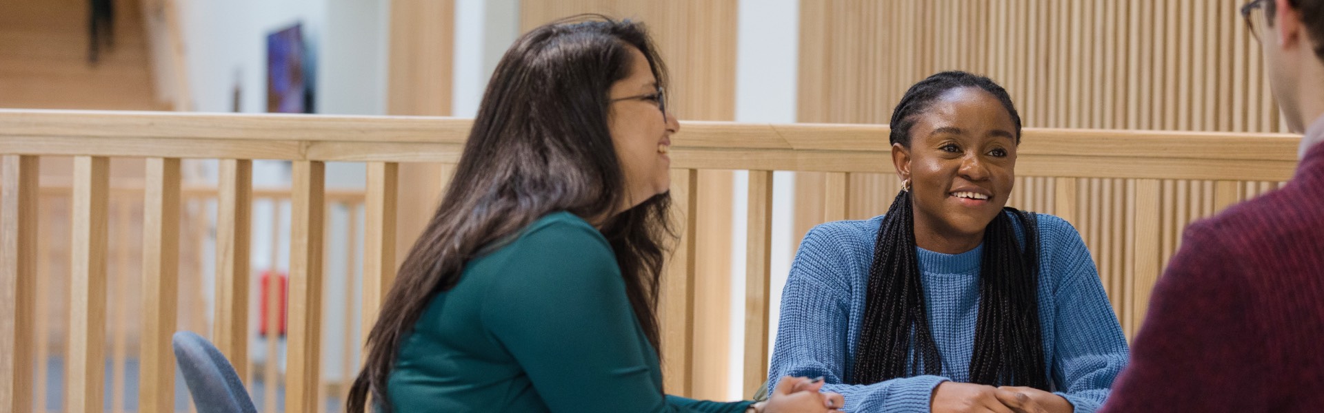 Three students sit at a table in the Management School atrium