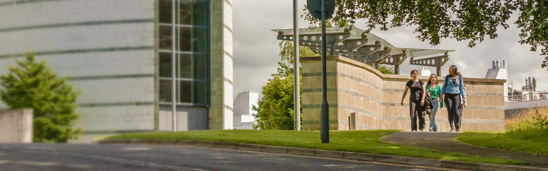 Three students walk on a footpath on the crest of a hill. A white building is in the background.