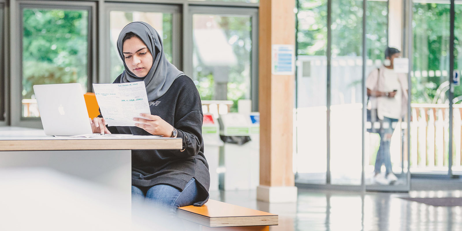 A student in a headscarf works at a laptop in the LICA foyer.