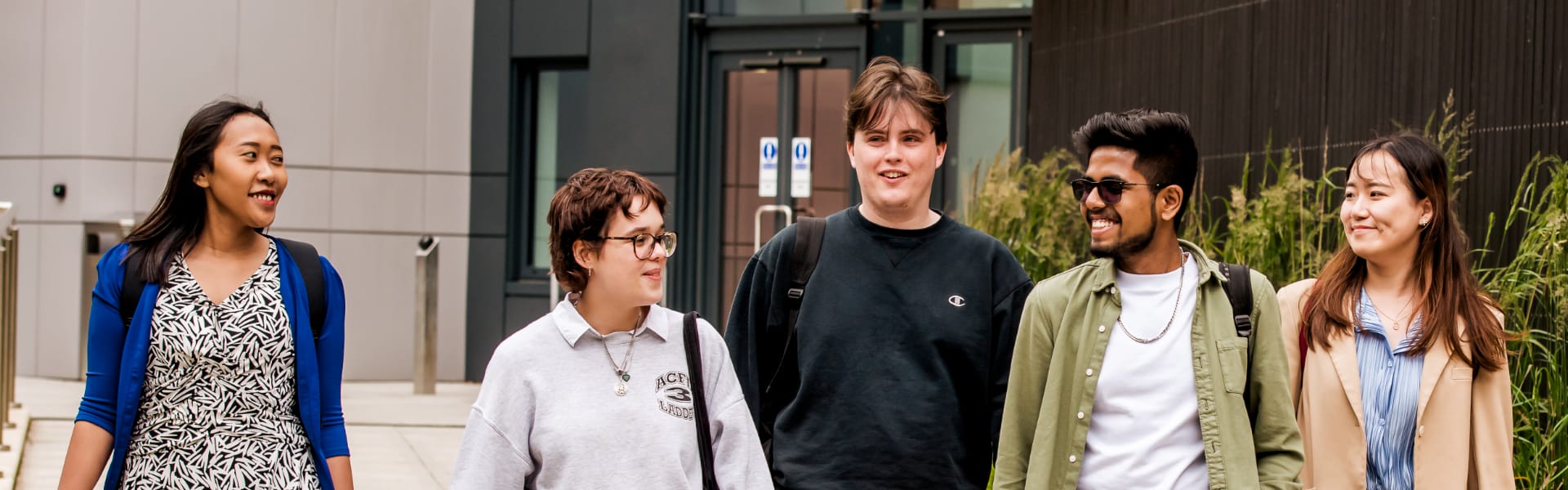 Five students walk on a path on the campus past modern buildings.