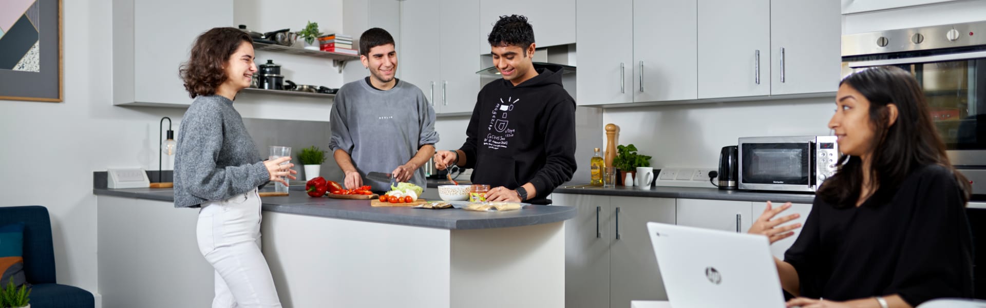 Students in the kitchen of an accommodation flat are chatting and cooking.