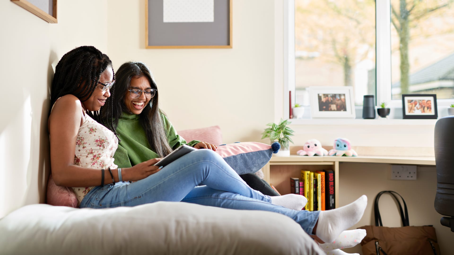 Two students sit on a bed in a student's bedroom