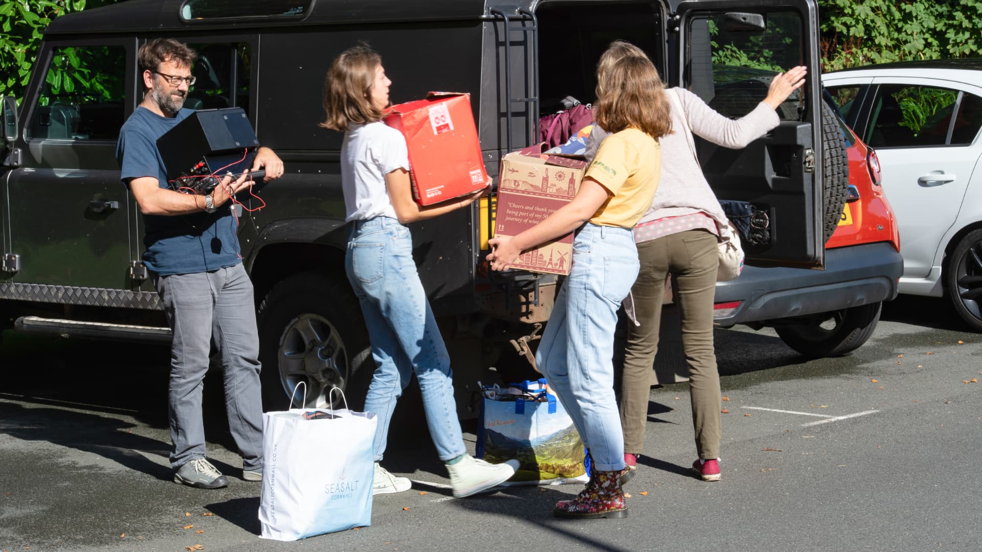 A family unload boxes from the back of a car.