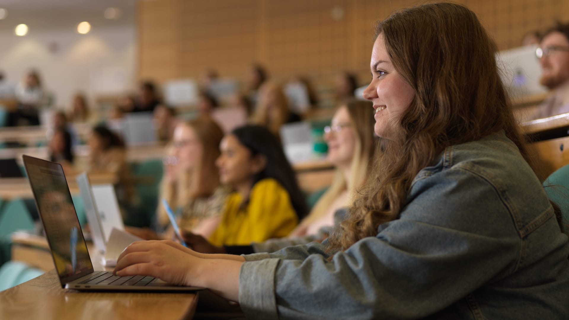 A student sits at a laptop in a lecture theatre