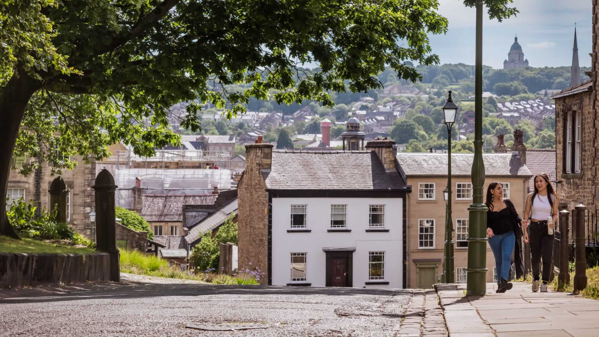 Two students walk on Lancaster's historic streets with the Ashton Memorial on a hill in the background.