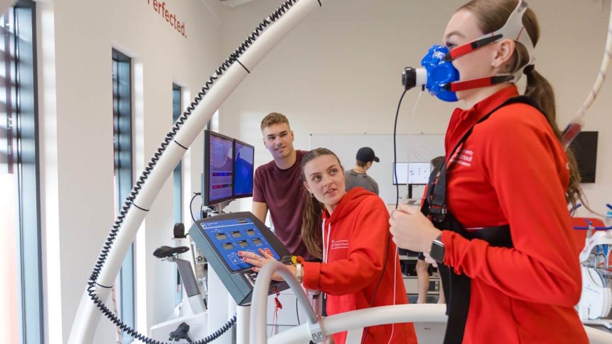 A student monitors the health of another student running on a treadmill.