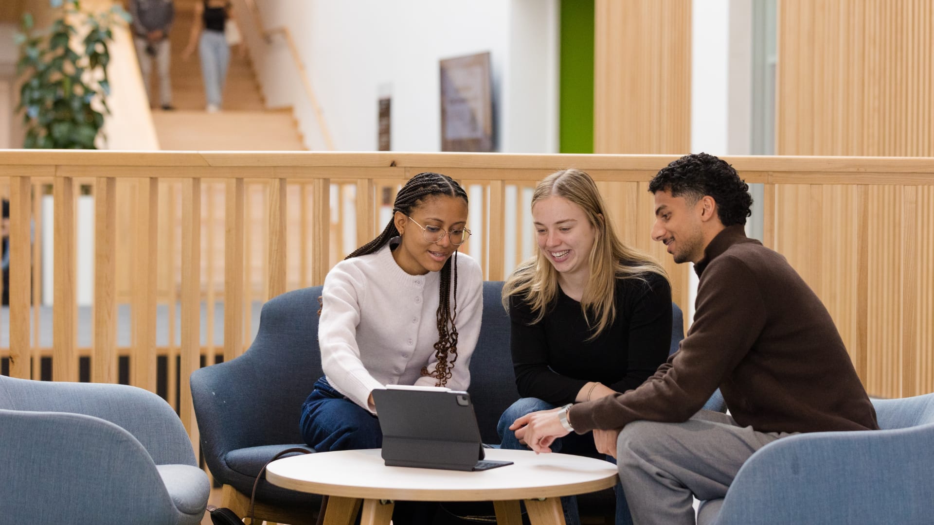 Three students discuss something on an iPad on a mezzanine in an atrium.