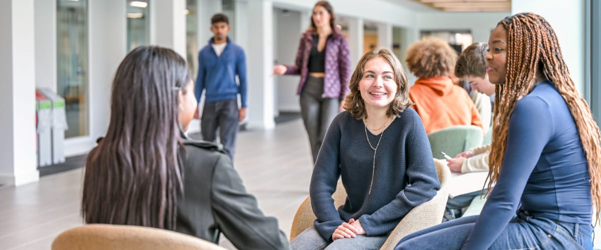 A trio of students sit laughing and chatting in a modern building.