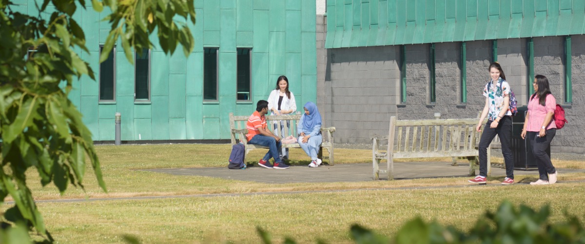 Students in groups stand outside Lancaster University's Infolab building in the sunshine.