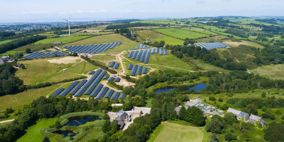 Lancaster's wind turbine and solar farm, pictured on green fields with Morecambe Bay and the Lake District in the distance.