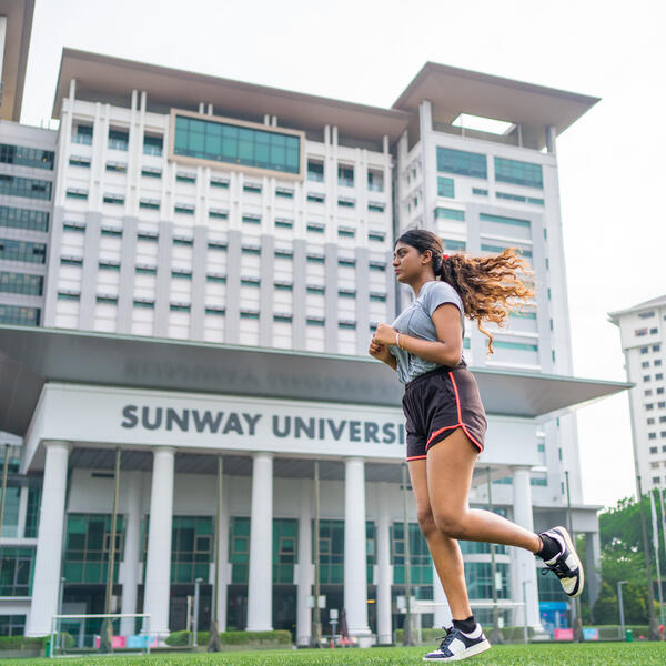 A student jogs past a large building of Sunway University campus